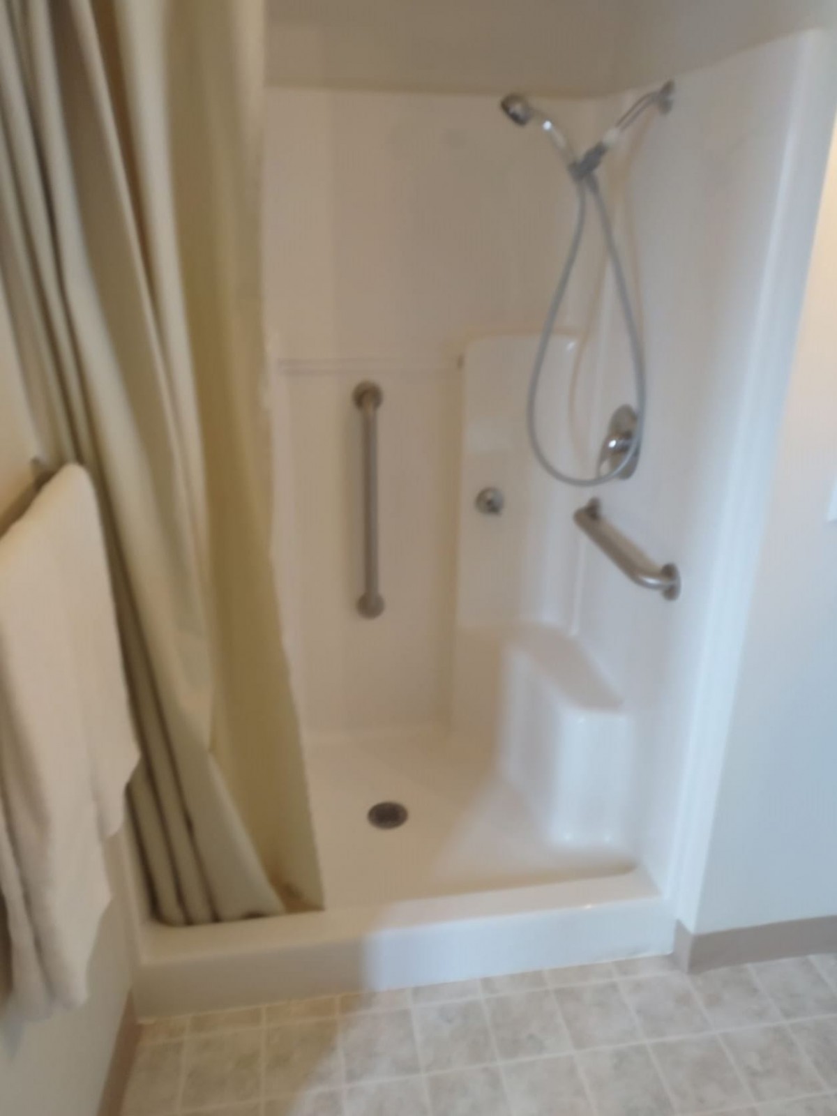 A bathroom with a shower and bathtub combination featuring grab bars and a handheld showerhead.