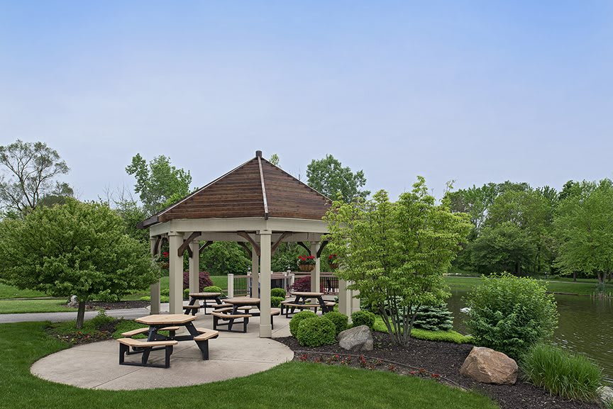 A scenic gazebo surrounded by picnic tables and lush greenery in a park setting.