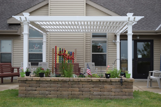 A cozy outdoor space featuring a white pergola, potted plants, and a decorative flag.