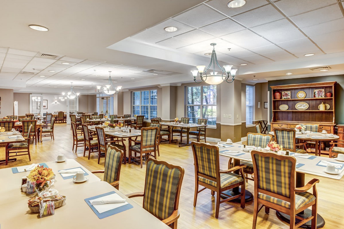 A spacious dining room with neatly arranged tables and chairs, featuring chandeliers and large windows.