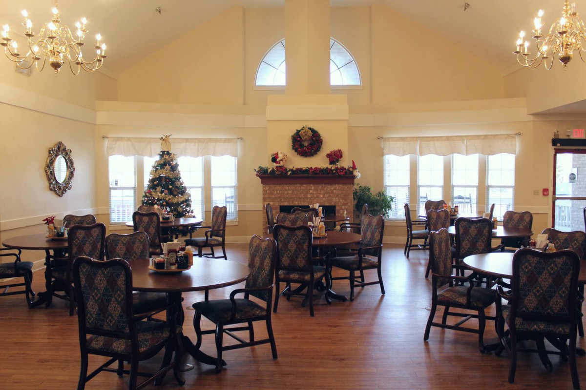 A cozy dining room with a festive Christmas tree and a warm fireplace surrounded by tables and chairs.