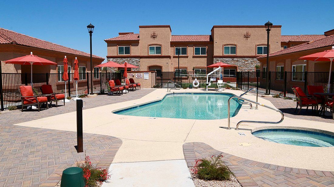An outdoor swimming pool area at a hotel, featuring umbrellas and lounge chairs under a clear blue sky.