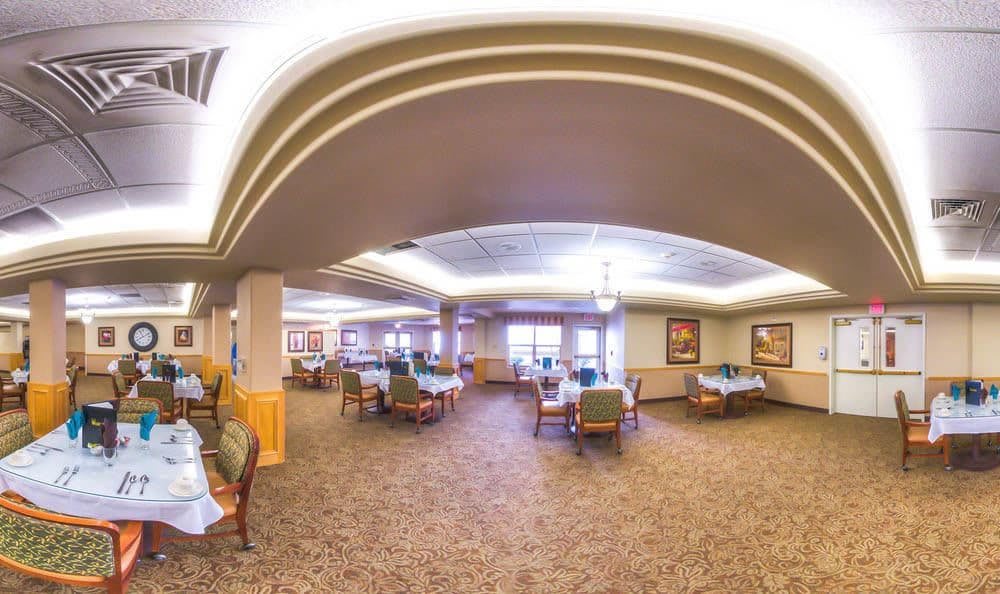 A spacious dining area with tables and chairs, featuring carpeted flooring and ceiling lights.