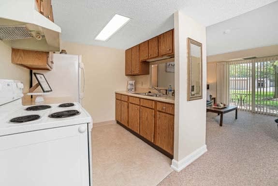 A compact kitchen area with wood cabinets and a stove, connected to a bright living space in an apartment.