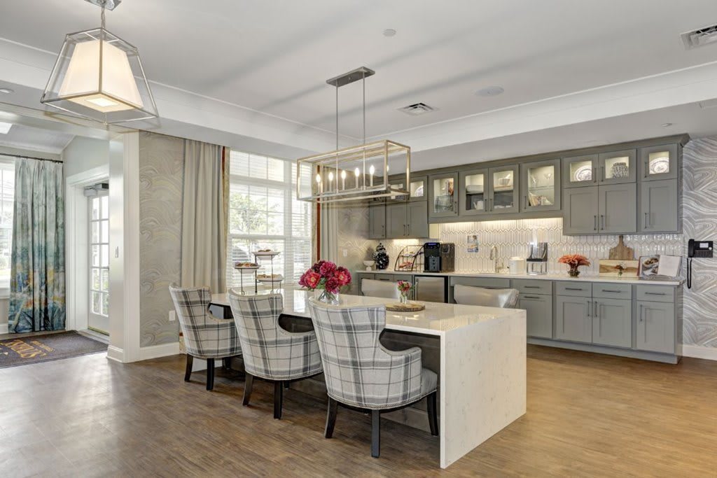 A modern kitchen with an island counter and stylish dining area, featuring gray cabinets and a chandelier.