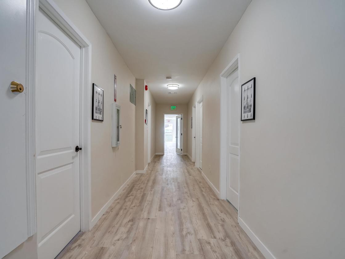 A long, well-lit hallway with multiple doors and framed artwork on the walls.