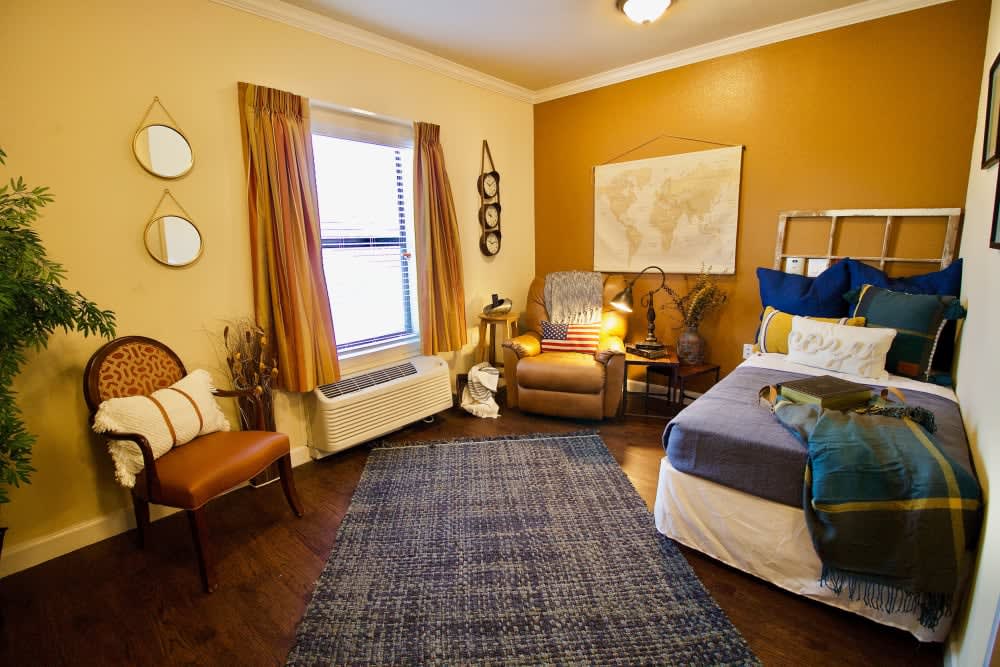 A cozy bedroom with warm colors, featuring an armchair and artwork on the walls.