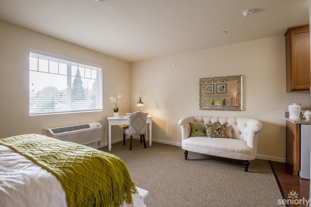 A cozy bedroom with a desk and sofa, decorated in soft neutral tones.