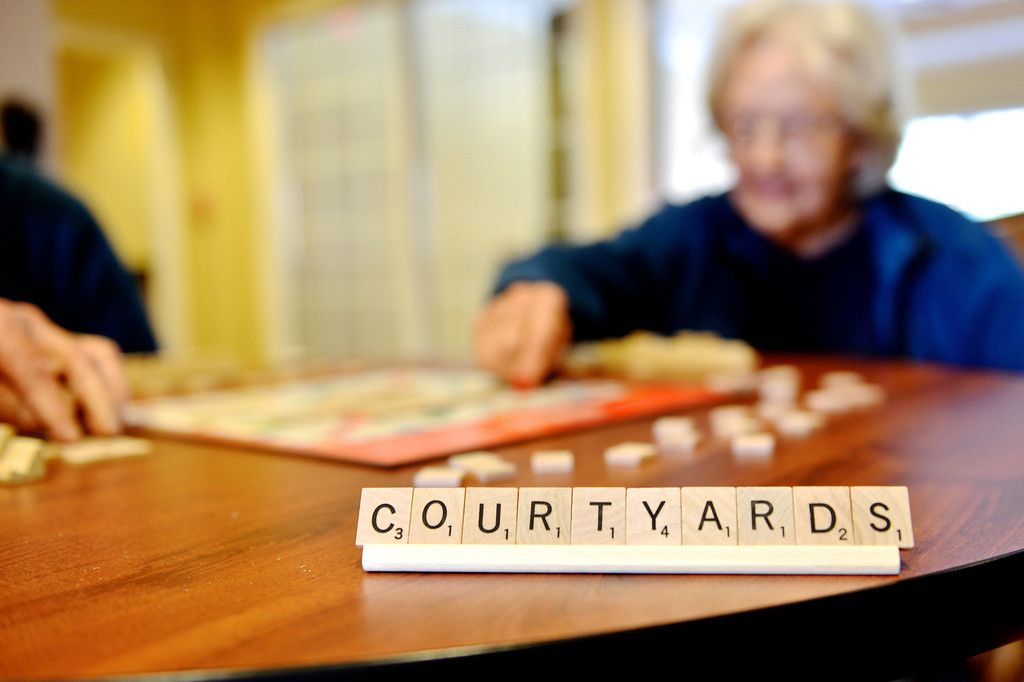 An elderly person playing Scrabble, with the word 'courtyard' displayed on the rack.