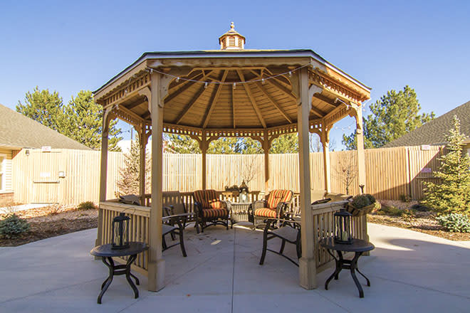 A wooden gazebo with outdoor seating in a sunny backyard setting.