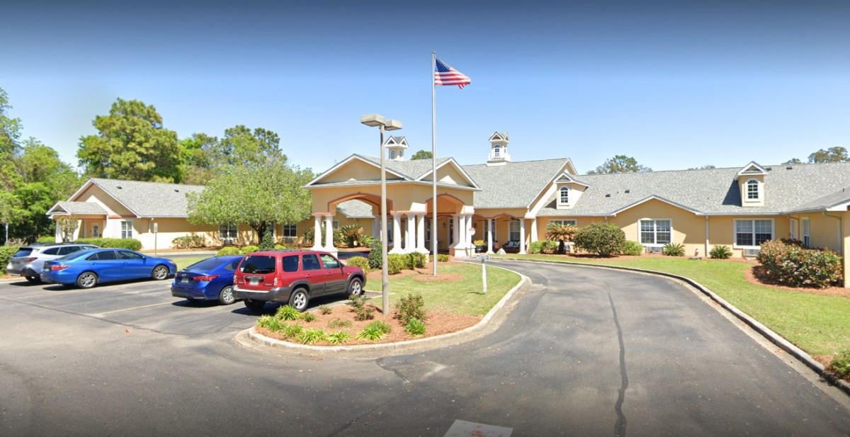 A building with a circular driveway and parking area, featuring a flagpole with an American flag.