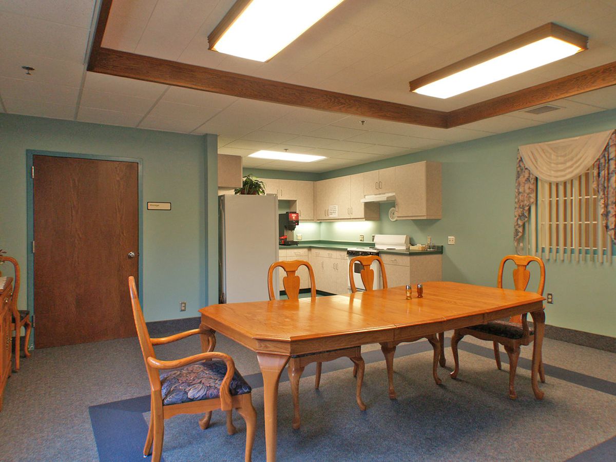 A well-lit dining area with a wooden table and chairs adjacent to a kitchen.