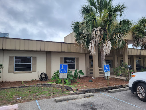 A view of a building with handicap accessible parking spaces and palm trees in the foreground under a cloudy sky.