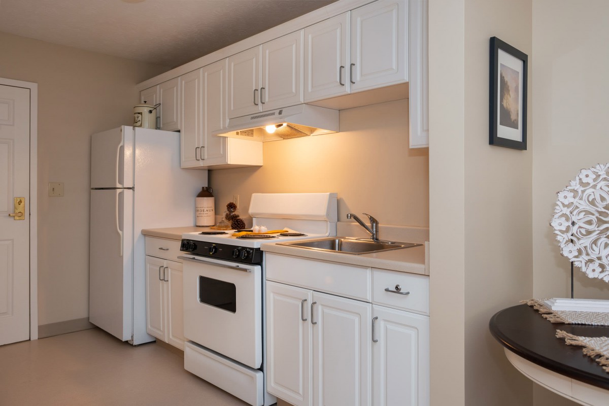 A compact kitchen with white cabinets, a stove, refrigerator, and sink.