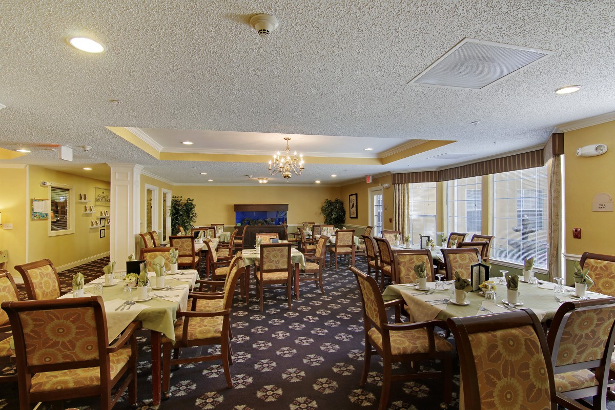 An elegant dining room with neatly arranged tables and chairs, featuring a chandelier and patterned carpet.