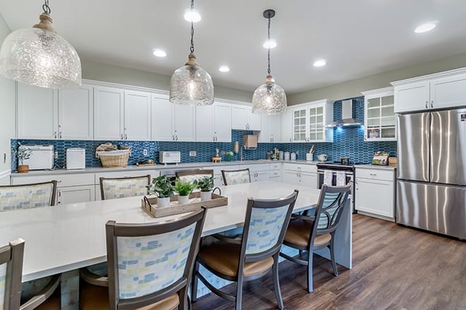 A modern kitchen with white cabinets, blue backsplash, and a spacious dining area.