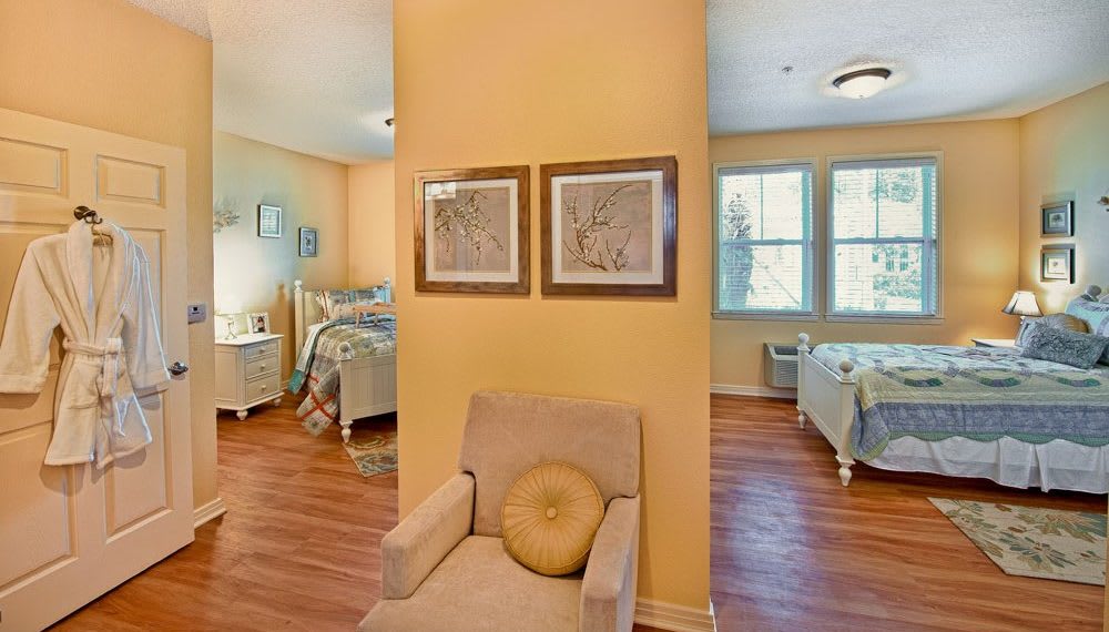 A cozy bedroom with yellow walls features two twin beds and wooden flooring, divided by a small seating area with framed artwork on the wall.