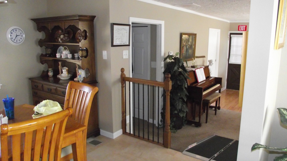 A cozy living room featuring a wooden chair, a piano, and a decorative shelf with a baby gate in the doorway.
