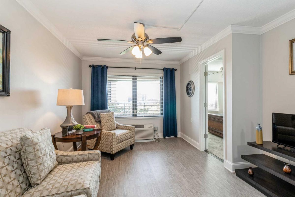 A cozy living room with armchairs, a lamp, and large windows with blue curtains.