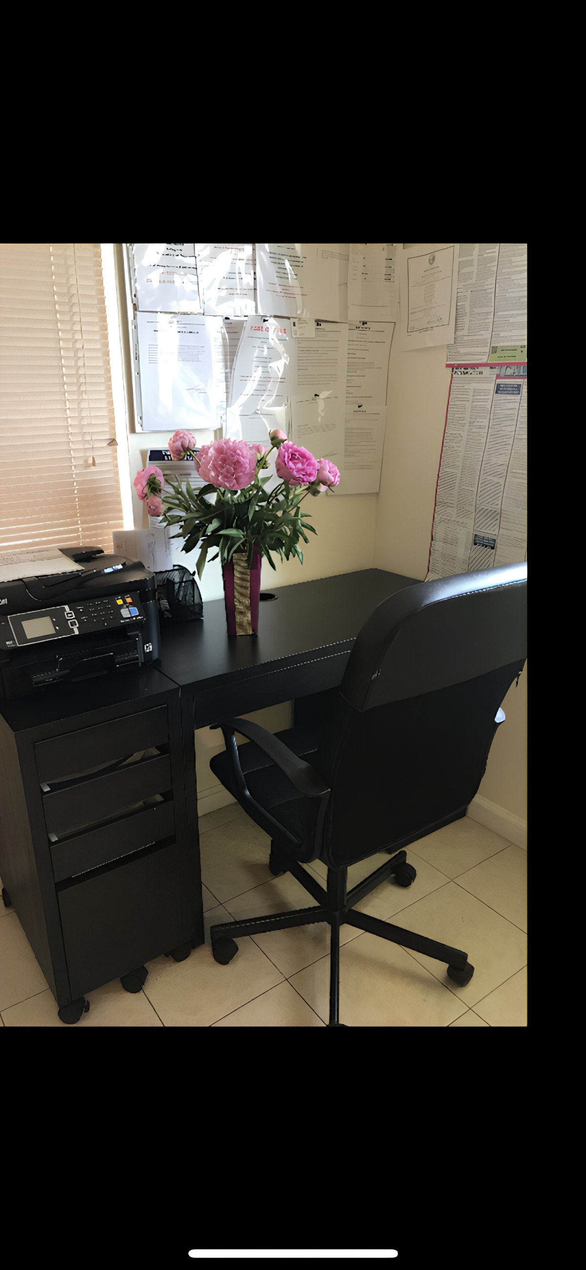 A tidy office setup with a desk, chair, printer, and a vase of flowers.