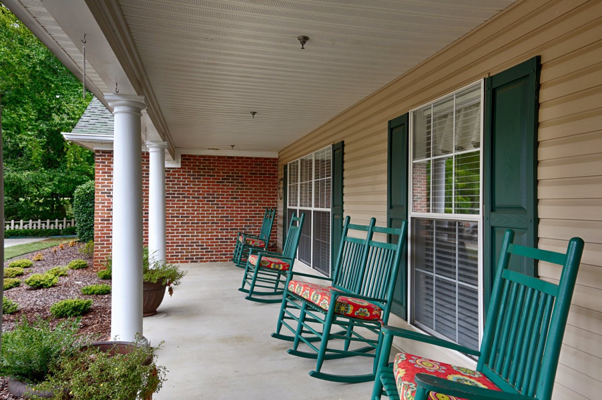 A cozy porch with green rocking chairs and cushioned seats.