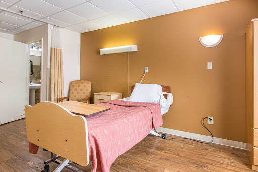 A clean and well-lit hospital patient room with a bed, armchair, and bedside lighting.
