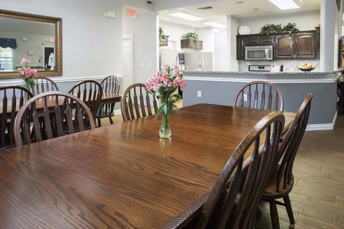 A cozy dining area featuring a wooden table and chairs, with a vase of flowers as the centerpiece, adjacent to a modern kitchen.