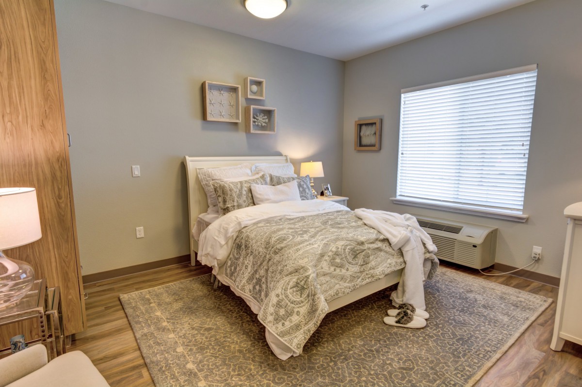 A cozy bedroom featuring a neatly made bed with patterned bedding, soft lighting from a bedside lamp, and wall art for decoration.