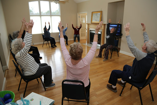 A group of seniors participating in a seated exercise class, raising their hands in unison.