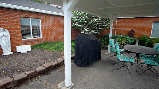 A covered grill sitting on a patio beside some outdoor seating and greenery.