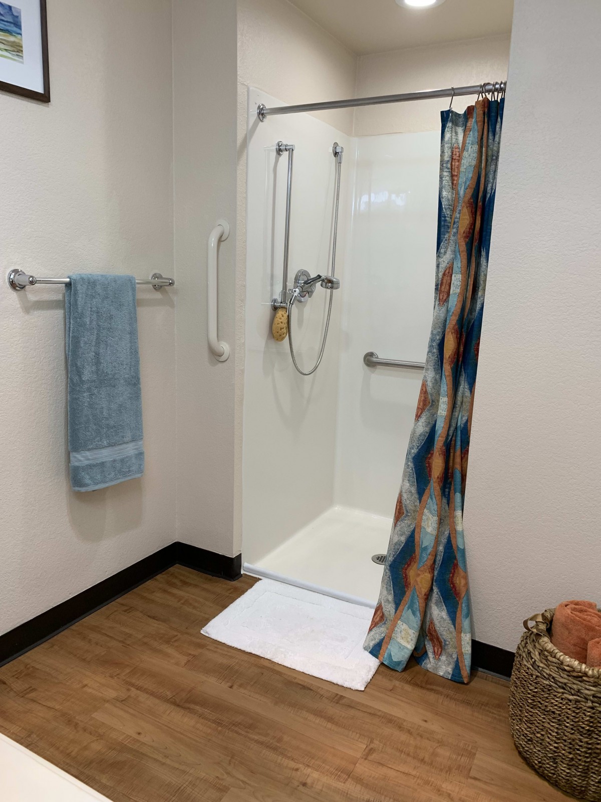A bathroom featuring a walk-in shower with grab bars, a colorful shower curtain, and a towel hanging on the wall.