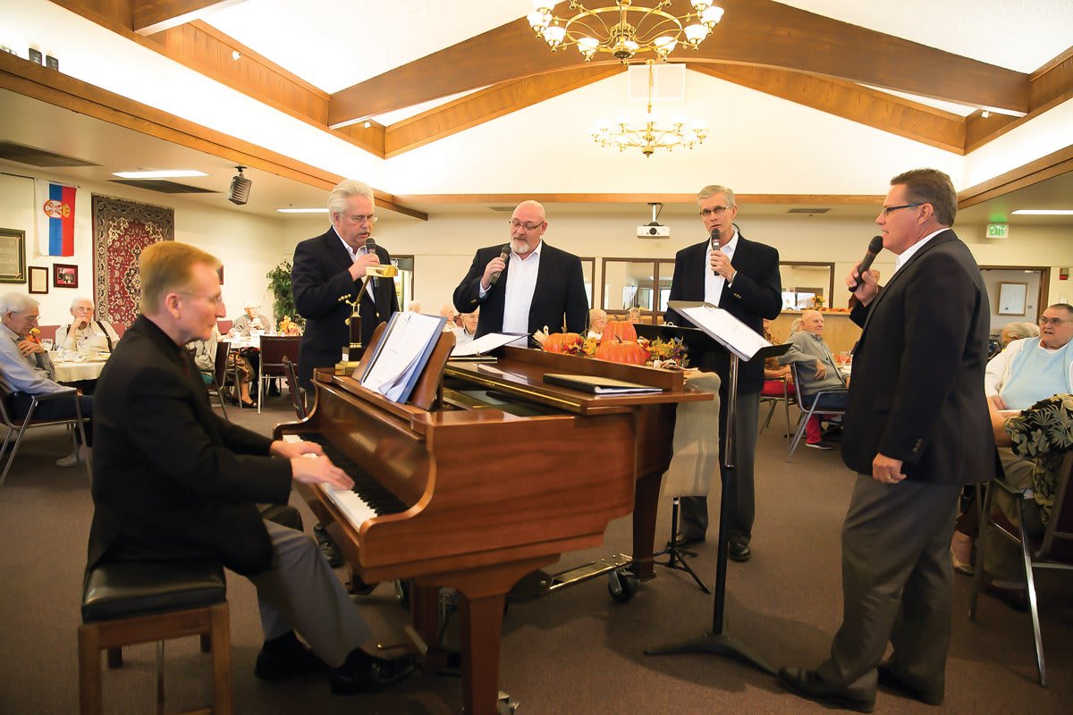 A group of musicians performing indoors, featuring a pianist and singers.
