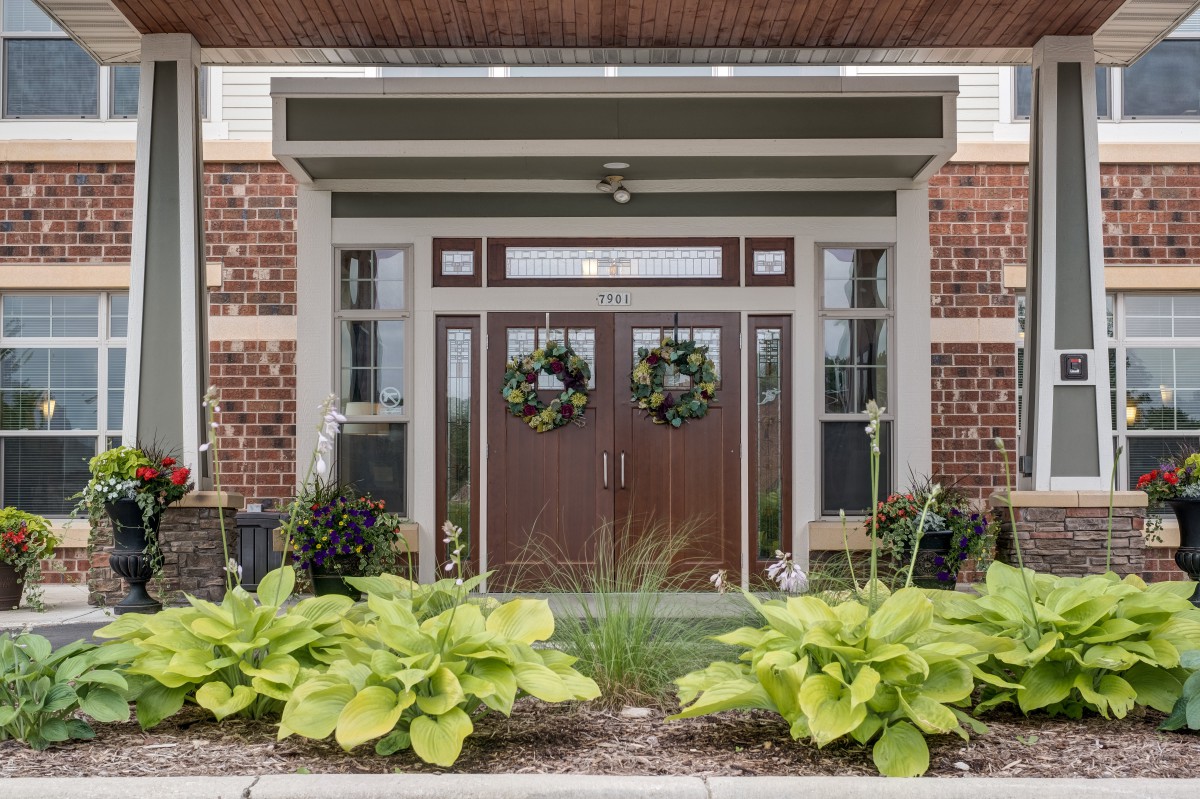 A welcoming entrance with double doors adorned with wreaths, surrounded by lush greenery and brickwork.