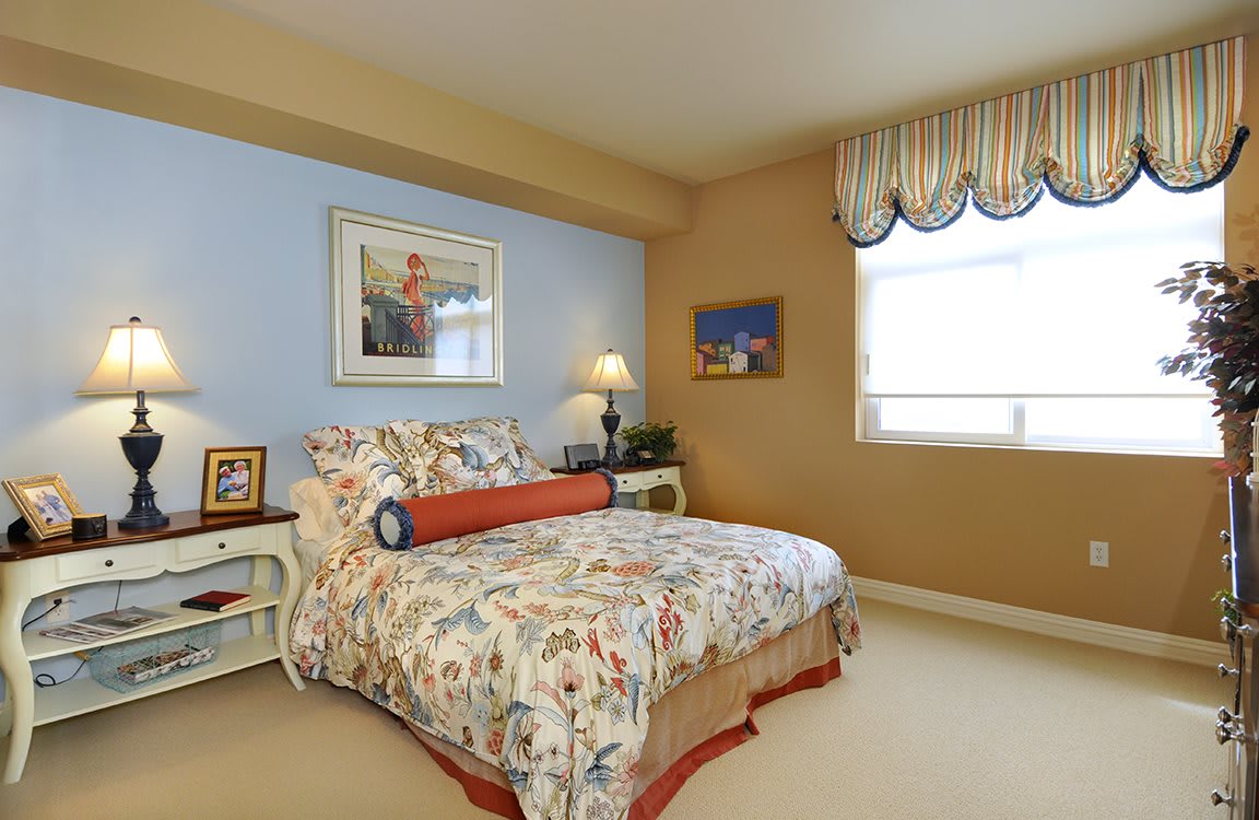 A cozy bedroom with floral bedding and decorative wall art, complemented by a nightstand and table lamp.
