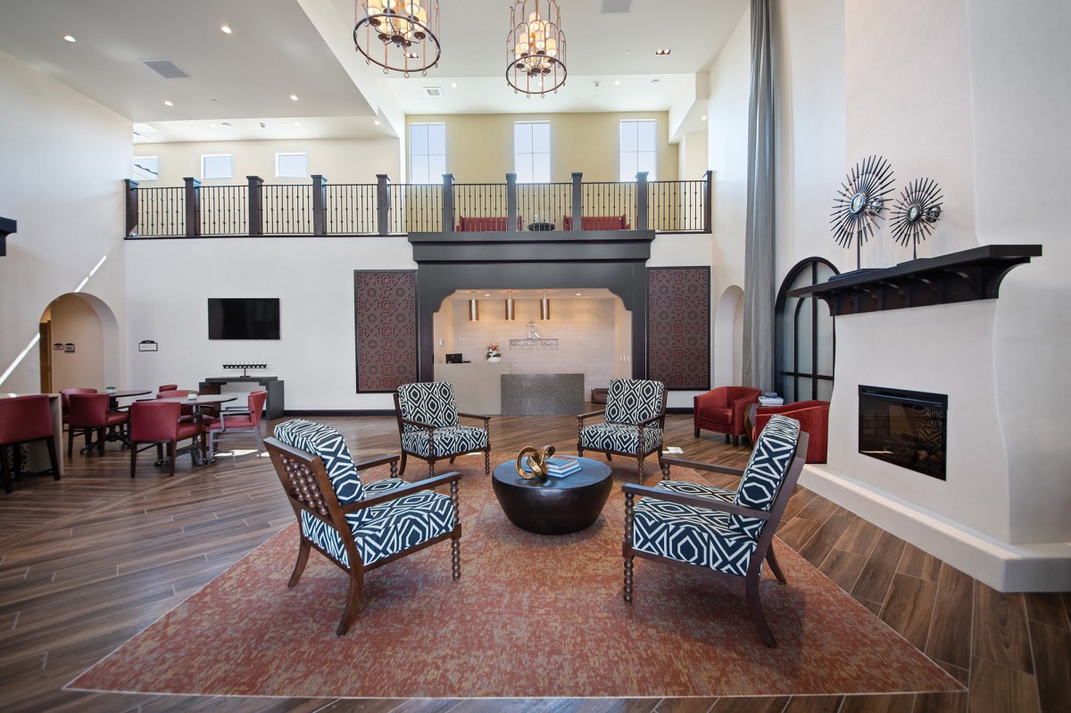 A modern living room with a loft, featuring stylish chairs, chandeliers, and a fireplace.