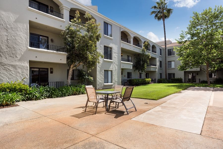 A well-maintained apartment building with a courtyard featuring outdoor seating and palm trees.