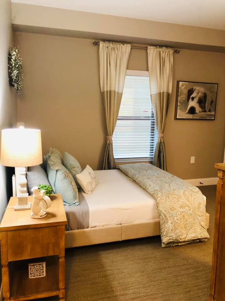 A cozy and well-decorated bedroom with a neatly made bed, side table with a lamp, and artwork on the wall.