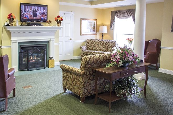 A cozy living room with patterned sofas, a coffee table with flowers, and a fireplace under a mounted television.