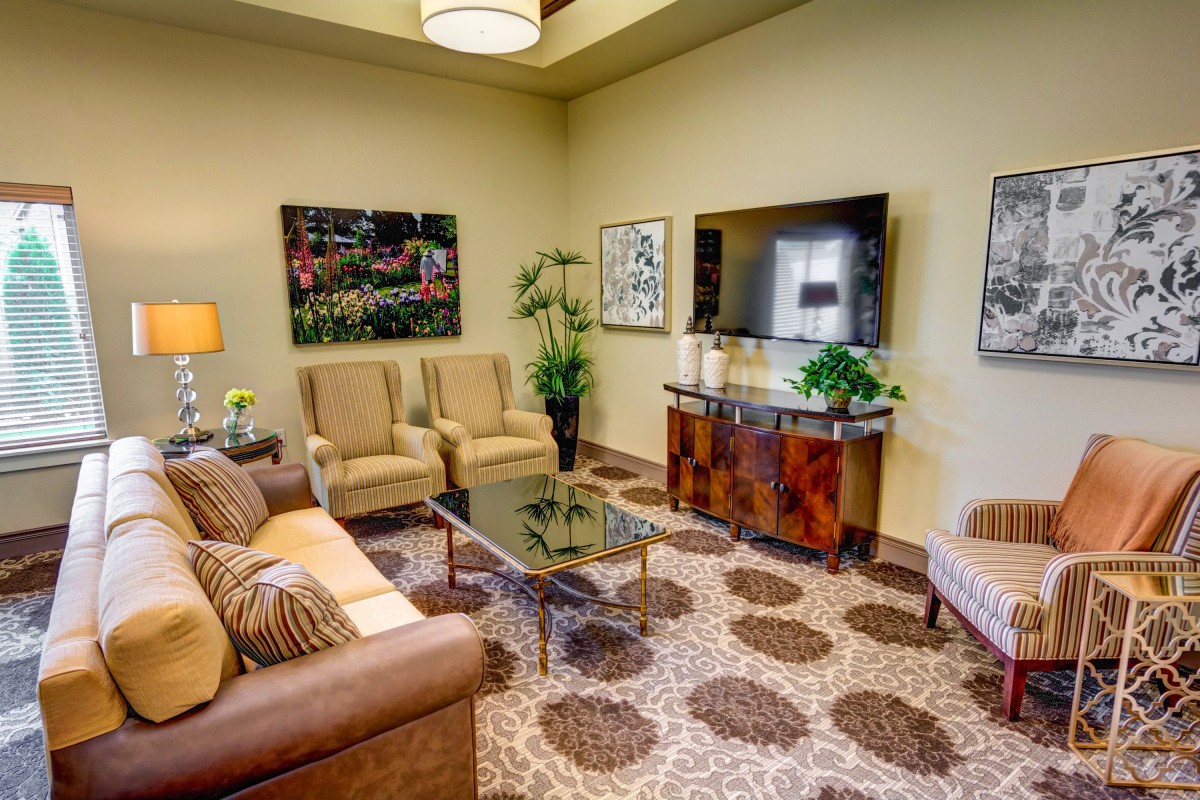 A cozy living room featuring a sofa, armchairs, coffee table, and wall-mounted TV, accented with plants and artwork.