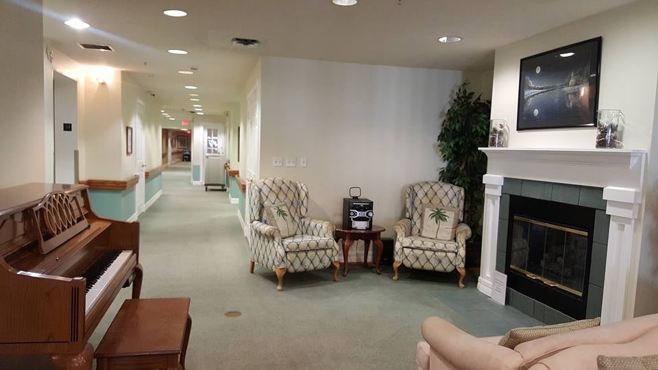 A cozy lobby area with patterned chairs, a small table, and a fireplace along a hallway.