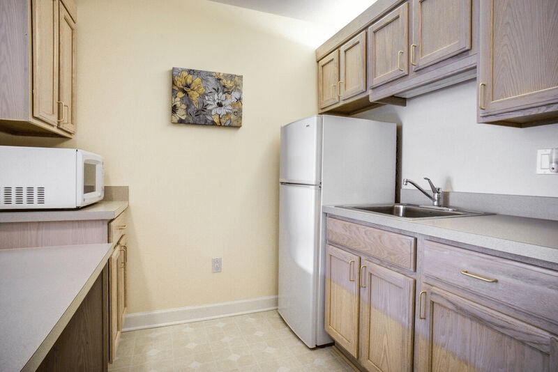 A small kitchen area with wooden cabinets, a refrigerator, and a countertop sink.