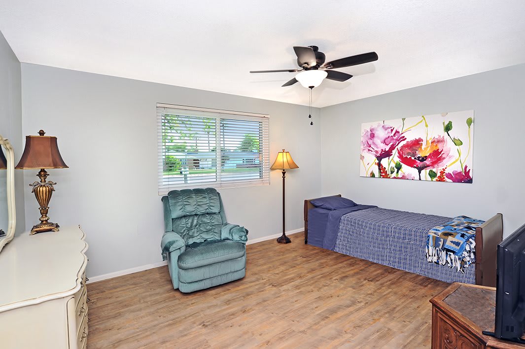 A cozy bedroom featuring an armchair, single bed, and floral wall art, with natural light coming in through the window.