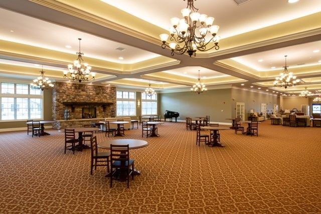A spacious banquet hall with elegant chandeliers, carpeted flooring, and neatly arranged tables and chairs.