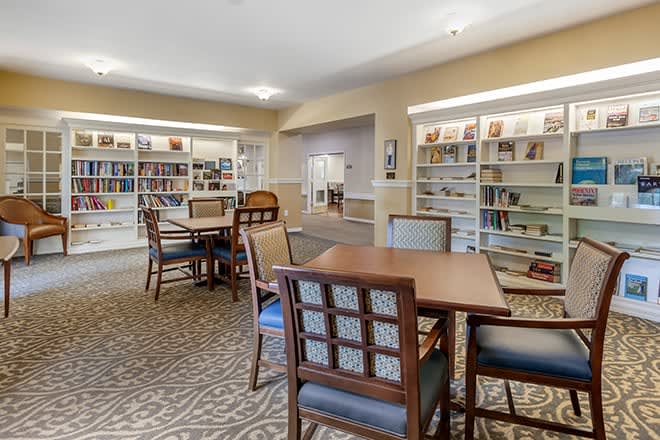 A cozy library interior with tables and chairs surrounded by bookshelves.