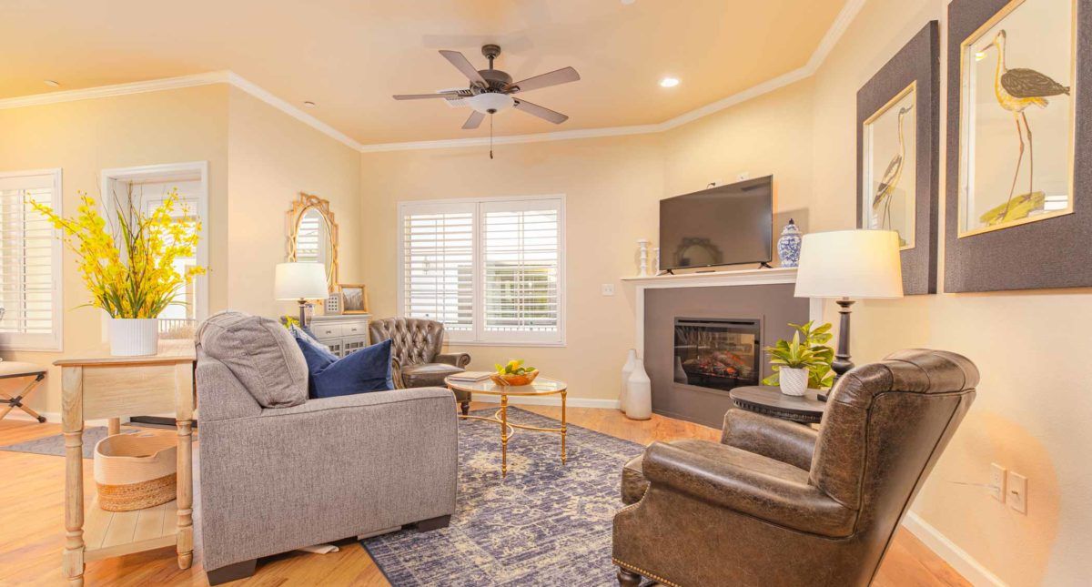 A cozy living room with a sofa, armchairs, and a fireplace, featuring a TV above the mantel.
