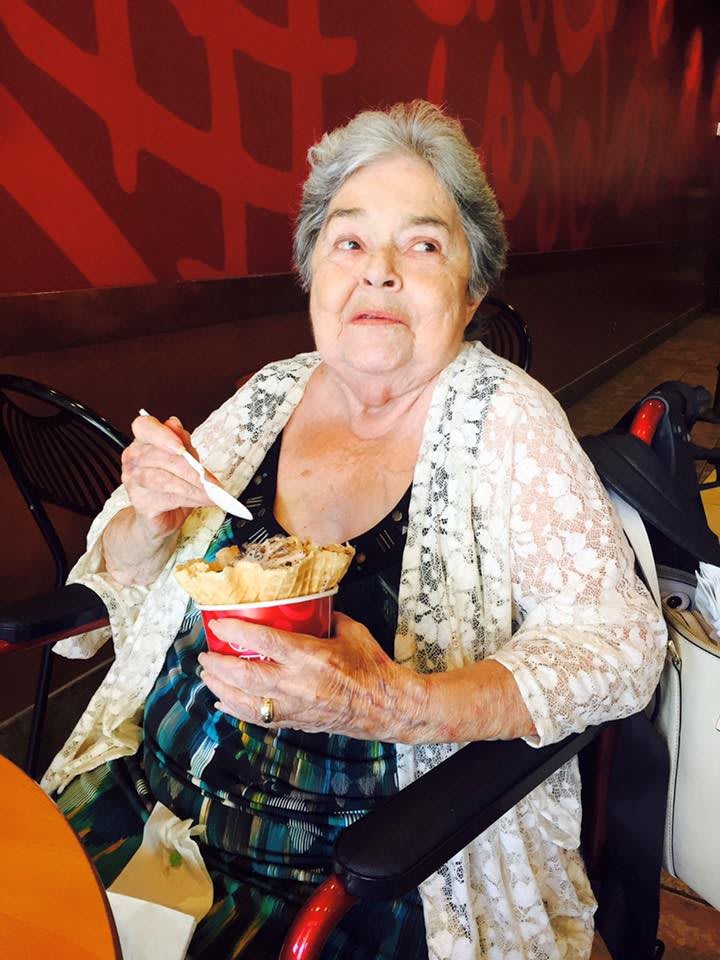 An elderly woman enjoys a cup of ice cream indoors.