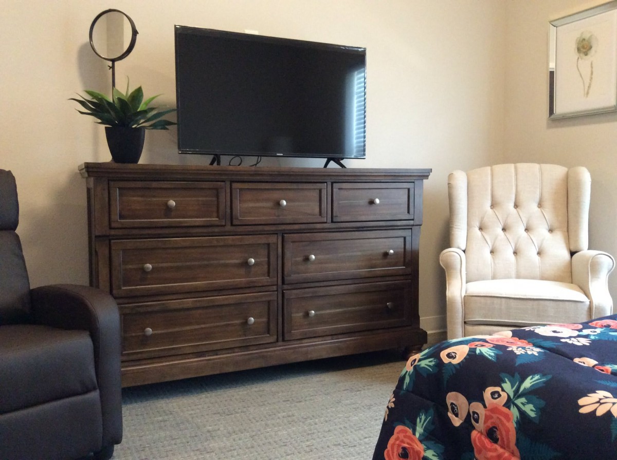 A cozy bedroom setup with a wooden dresser, television, and an upholstered chair.