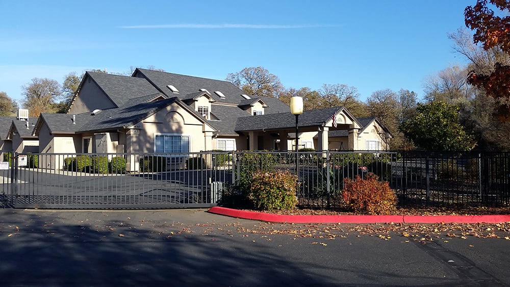 A large residential building with a fenced entrance and surrounding trees.