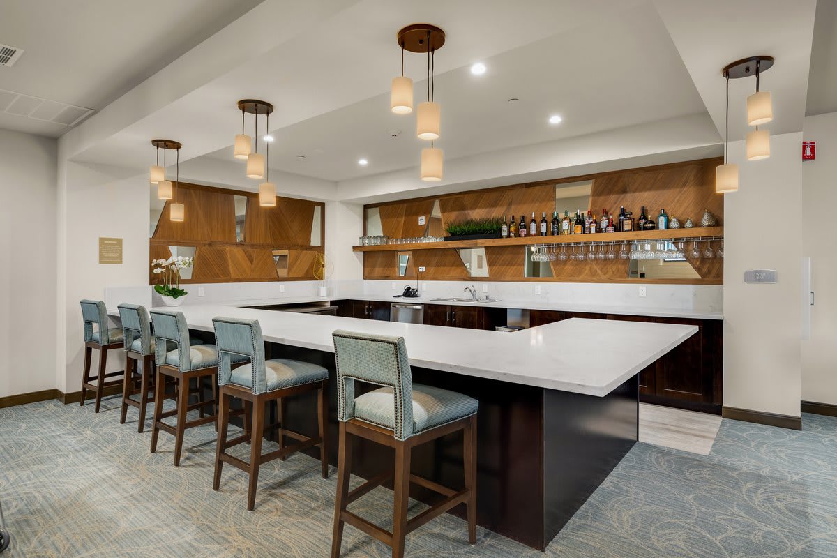 A modern bar with a sleek countertop, stylish stools, and warm lighting.