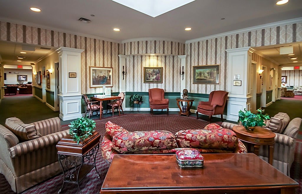 A traditional living room with striped wallpaper, featuring a sofa, armchairs, a coffee table, and framed artwork.